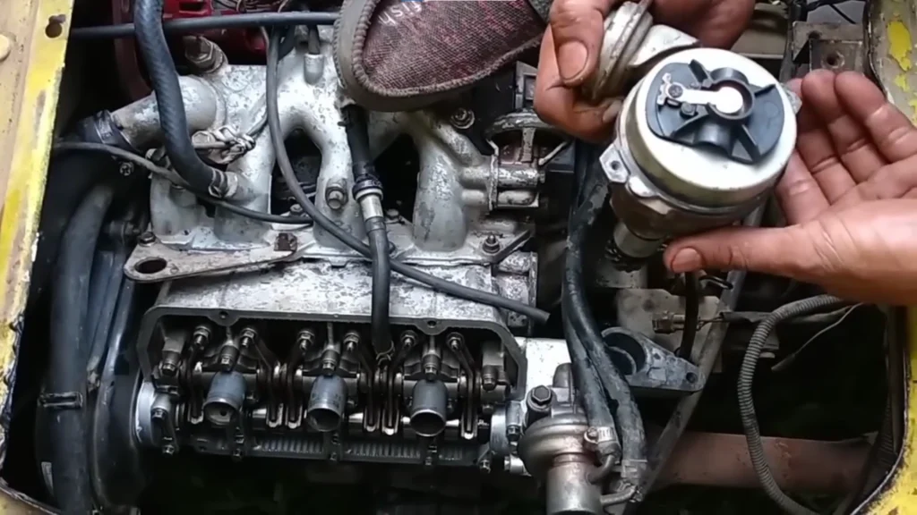 How to Time and Reinstall the Distributor on a Suzuki Multicab F6A Engine 3 Close-up of a Suzuki Multicab F6A engine bay with the valve cover removed, showing the rocker arms while a mechanic holds the distributor assembly beside the cylinder head for inspection.