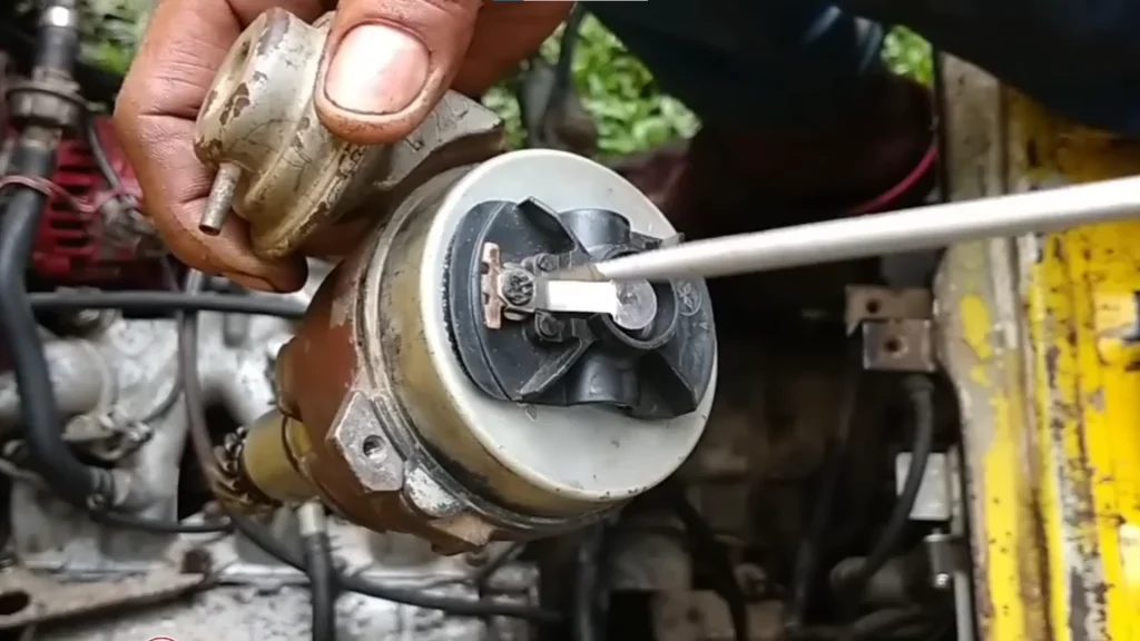 How to Time and Reinstall the Distributor on a Suzuki Multicab F6A Engine 2 Close-up of a Suzuki Multicab F6A distributor assembly being held near the engine bay while a screwdriver points to the internal rotor and contact area.