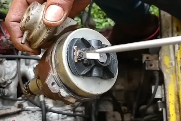 Close-up of a Suzuki Multicab F6A distributor assembly being held near the engine bay while a screwdriver points to the internal rotor and contact area.