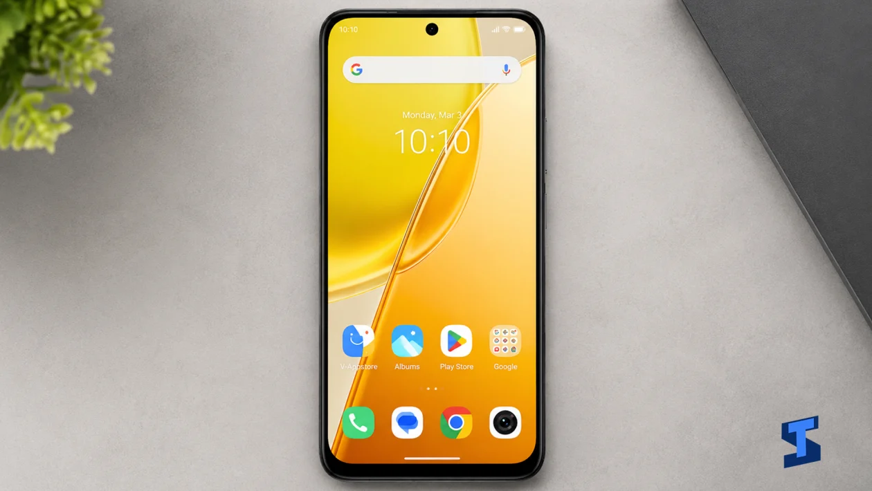 vivo Y51 Pro lying flat on a clean gray tech table in an overhead shot, showing its bright yellow-orange Home screen, centered punch-hole camera, slim black frame, app icons, Google search bar, and a softly blurred small plant in the corner.